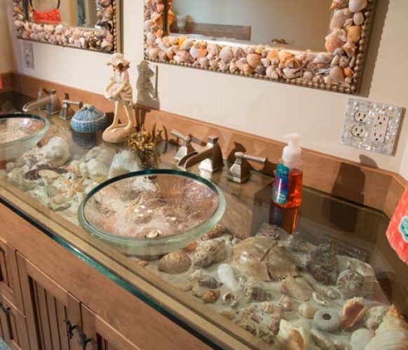 Jim Schopf, Andrea’s husband, designed the double vanity. The board over the cabinet doors flips down, allowing Andrea to switch shells in and out of the sand-covered shelf. Andrea created the shell-embellished mirrors.